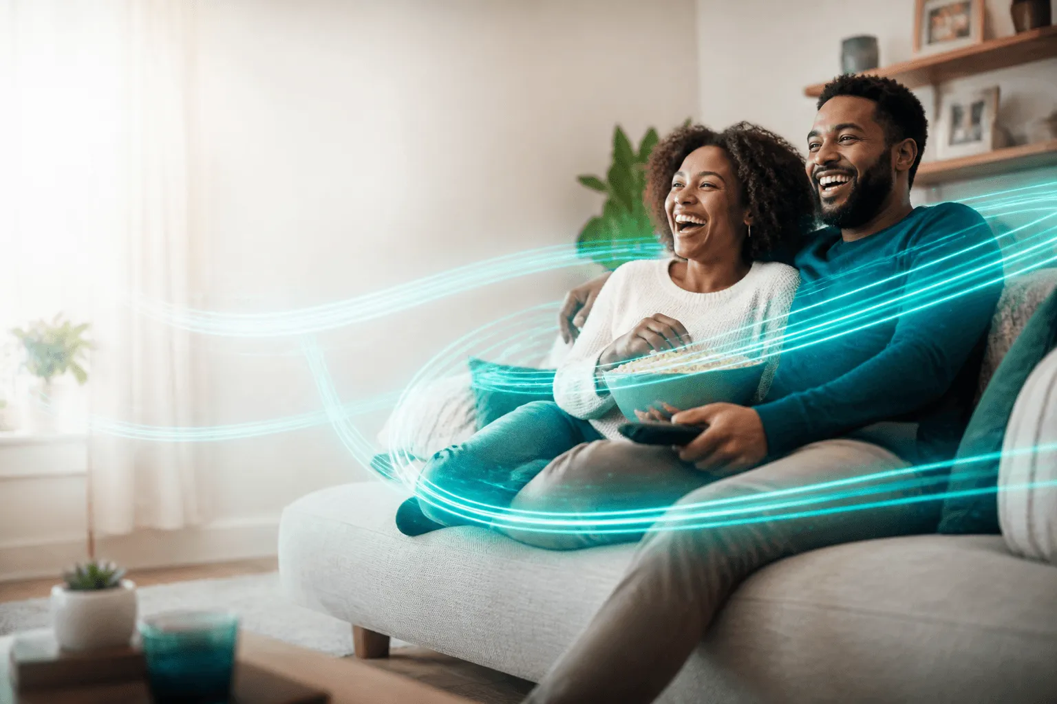 Two people laughing on a sofa while streaming, wrapped in ribbons of teal fiber light.